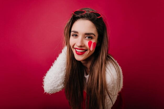 Beata ragazza romantica in posa con un sorriso sincero e giocando con i suoi capelli