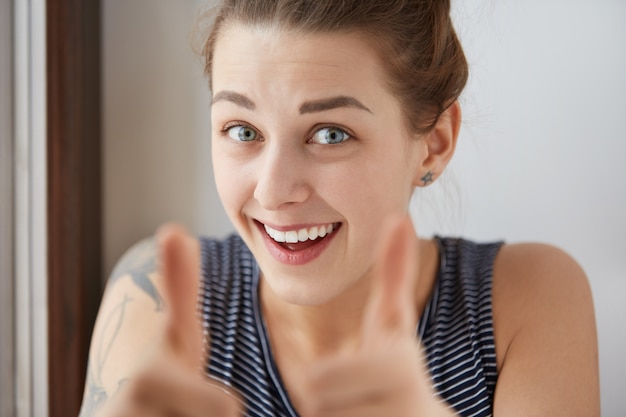 Bel colpo di affascinante donna dagli occhi azzurri con la bocca leggermente aperta. Attraente giovane studentessa ha felicemente superato tutti gli esami, mostrando i pollici in su come segni del suo felice successo. Buon risultato.