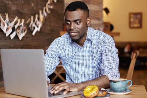 Bel giovane africano libero professionista che lavora al computer portatile in remoto