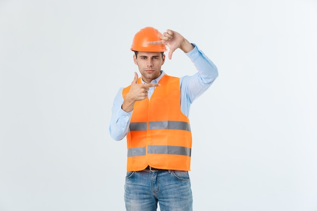 Bel giovane architetto uomo con indossare il casco di sicurezza su sfondo isolato rendendo il telaio con le mani e le dita con la faccia felice. Creatività e concetto di fotografia.