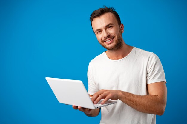 Bel giovane che usa il suo computer portatile su sfondo blu