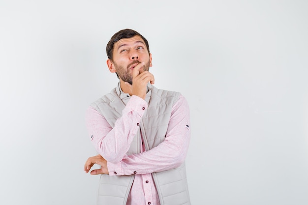 Bel giovane maschio con la mano sul mento, alzando lo sguardo in camicia, gilet e guardando premuroso, vista frontale.