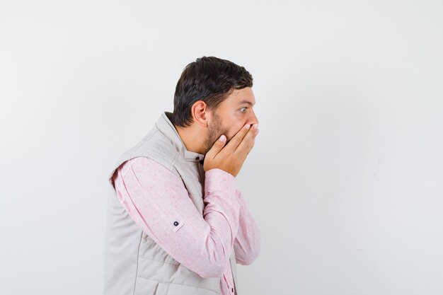 Bel giovane maschio con le mani sulla bocca in camicia, gilet e sembra scioccato.