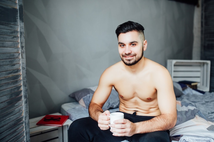 Foto gratuito bel giovane sexy sdraiato a torso nudo sul letto, con in mano una tazza di caffè
