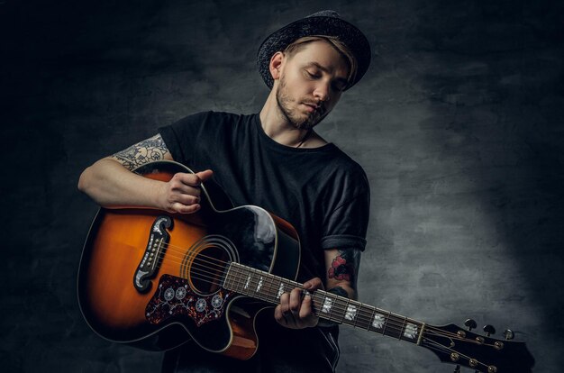 Bel giovane suonatore di blues di chitarra acustica con tatuaggi sulle braccia che esegue le sue abilità musicali.