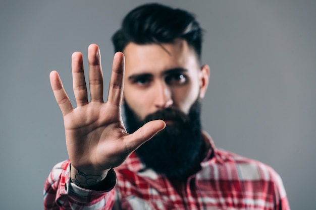 Bel giovane uomo barbuto sta tenendo la mano sulla barba e guarda lontano, su un muro grigio