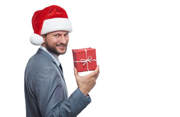 bel giovane uomo d'affari con la barba in un cappello di Natale che mostra un piccolo regalo di Natale sorridendo con gioia