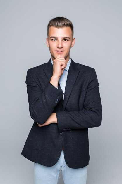 Bel giovane uomo in camicia e jeans tiene il braccio sotto il mento isolato su bianco