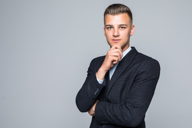 Bel giovane uomo in camicia e jeans tiene il braccio sotto il mento isolato su bianco