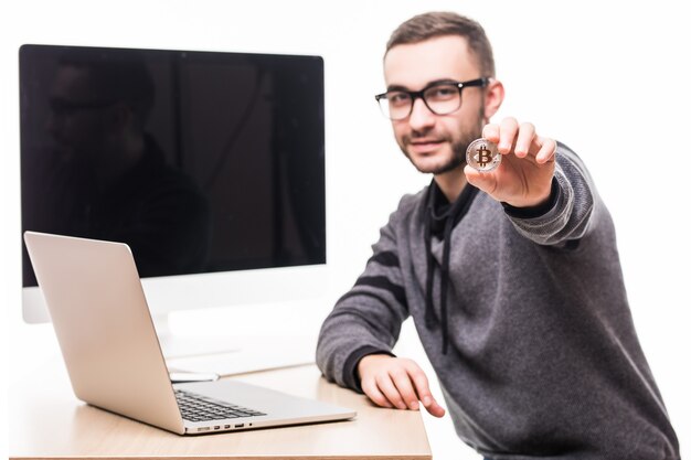 Bel giovane uomo seduto al posto dell'ufficio con il computer portatile e lo schermo del monitor sulla schiena puntava bitcoin su bianco