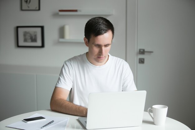 Bel giovane uomo seduto alla scrivania a lavorare con il computer portatile