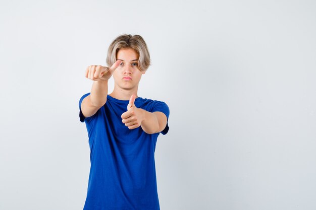 Bel ragazzo adolescente che mostra il doppio pollice in alto in maglietta blu e sembra sicuro. vista frontale.