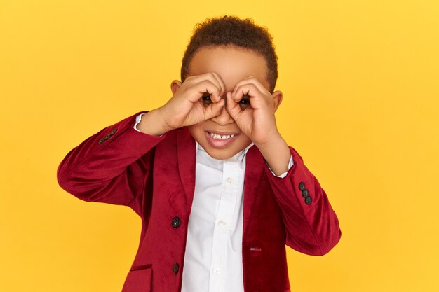 Bel ragazzo africano esaminando qualcosa utilizzando il binocolo esaminando la distanza. Curioso bambino dalla pelle scura snoopy spiando qualcuno che usa i vetri da campo.