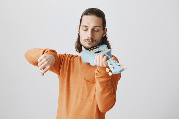Bel ragazzo divertente tenendo l'ukulele come il violino