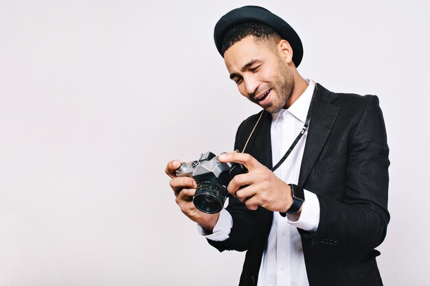 Bel ragazzo gioioso in tuta, cappello che guarda nelle mani. Viaggiare, turista, divertirsi, stile retrò, emozioni vere.