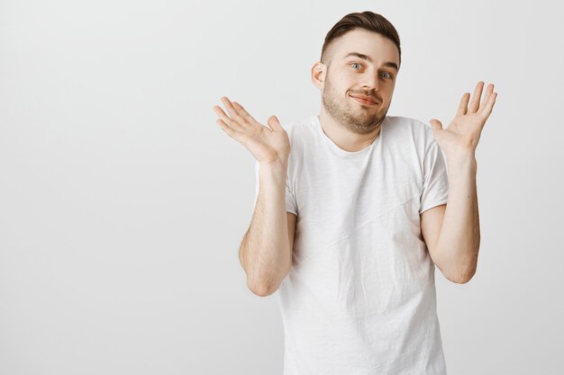 Bel ragazzo giovane che alza le mani e scrolla le spalle, non so niente, non ne ho idea, in piedi senza tracce