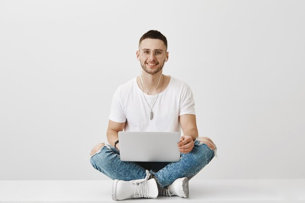 Bel ragazzo giovane sorridente con gli occhiali in posa con il suo computer portatile