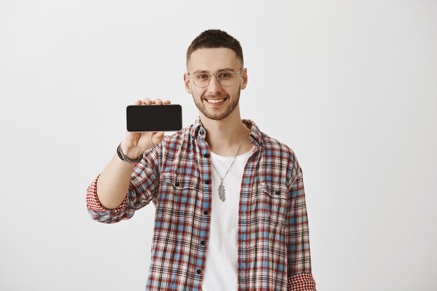 Bel ragazzo giovane sorridente con gli occhiali in posa con il suo telefono