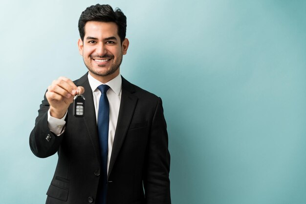 Bel venditore ispanico sorridente che consegna le chiavi di una nuova auto in studio