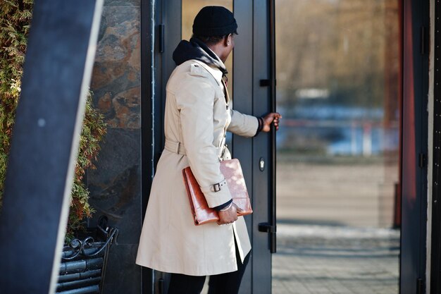 Bell'uomo afroamericano in posa fuori con cappello nero e cappotto beige con cartella in mano