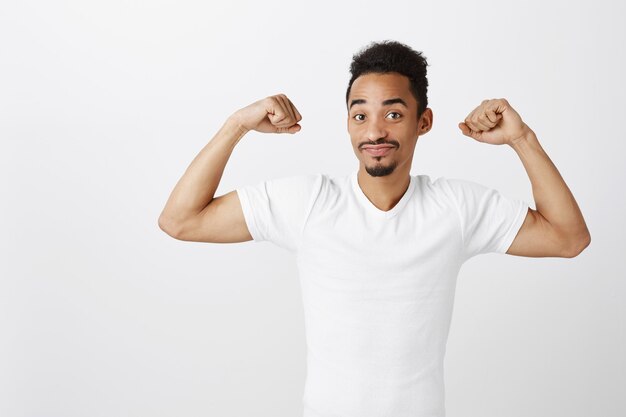 Bell'uomo afroamericano sicuro e forte che flette i bicipiti, allenamento in palestra, dall'aspetto impertinente