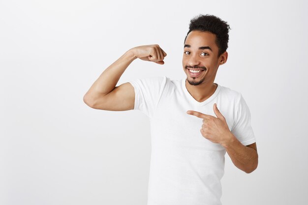 Bell'uomo afroamericano sicuro e forte che flette i bicipiti, allenamento in palestra, dall'aspetto impertinente