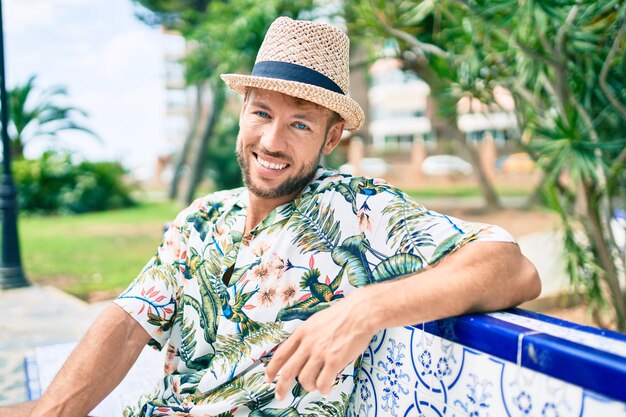 Bell'uomo caucasico che indossa cappello estivo e camicia di fiori che sorride felice all'aperto