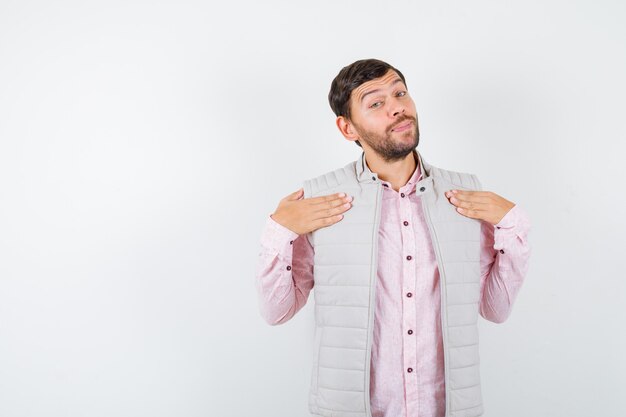 Bell'uomo che tiene le mani sul petto in gilet, camicia e sembra sicuro.