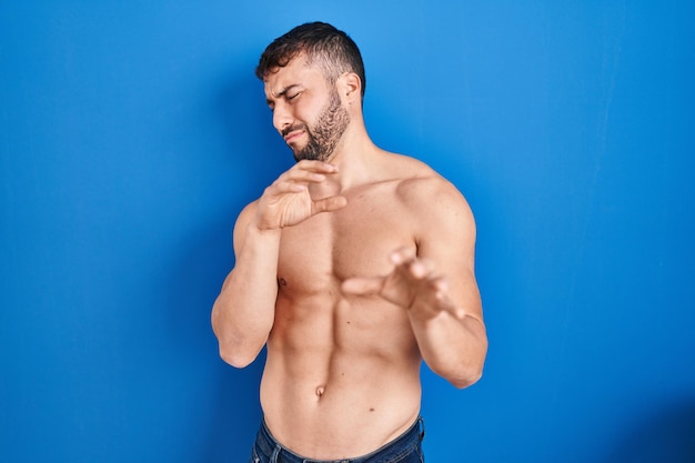 Bell'uomo ispanico in piedi espressione disgustata senza camicia, dispiaciuto e timoroso che fa la faccia disgustata a causa della reazione di avversione. con le mani alzate