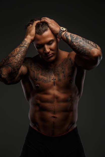 Bell'uomo muscoloso senza maglietta con tatuaggi sul corpo che tiene la testa. Isolato su sfondo grigio.