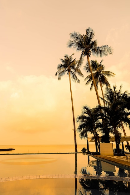 Bella alba con la palma di cocco della siluetta e la piscina della sedia intorno alla piscina nella bella stazione di lusso dell&#39;hotel - filtro dell&#39;annata
