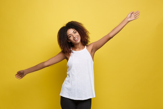 Bella attraente donna afroamericana postando giocare con i capelli ricci afro. Sfondo di studio giallo. Copia spazio.