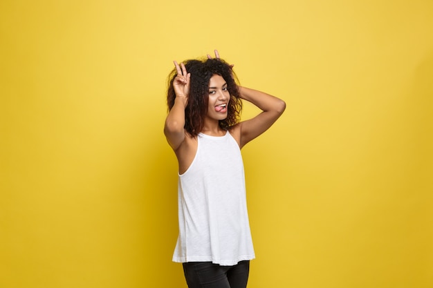 Bella attraente donna afroamericana postando giocare con i capelli ricci afro. Sfondo di studio giallo. Copia spazio.