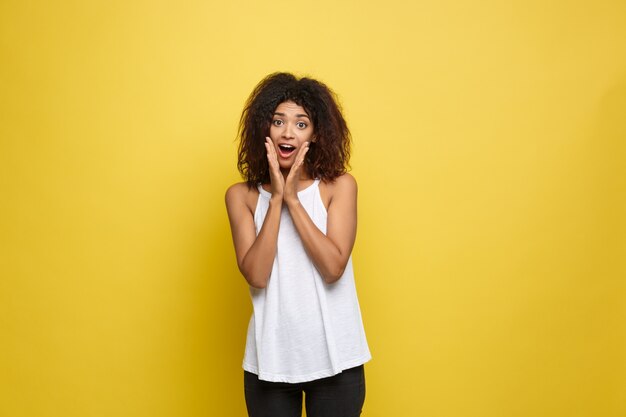 Bella attraente donna afroamericana postando giocare con i capelli ricci afro. Sfondo di studio giallo. Copia spazio.