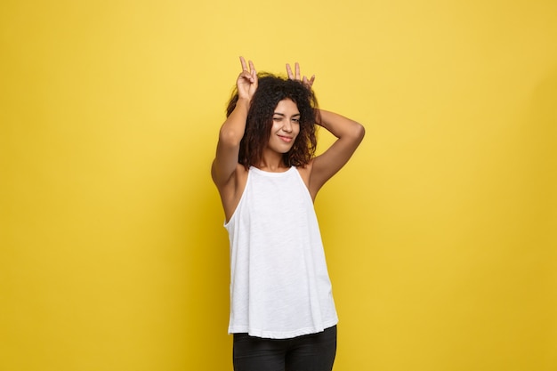 Bella attraente donna afroamericana postando giocare con i capelli ricci afro. Sfondo di studio giallo. Copia spazio.