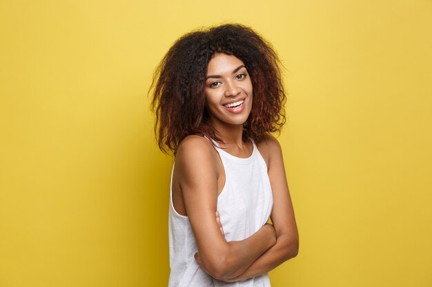 Bella attraente donna afroamericana postando giocare con i capelli ricci afro. Sfondo di studio giallo. Copia spazio.