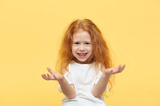 Bella bambina alla moda con lunghi capelli rossi che tiene i palmi aperti di fronte a lei come se tenesse un oggetto invisibile