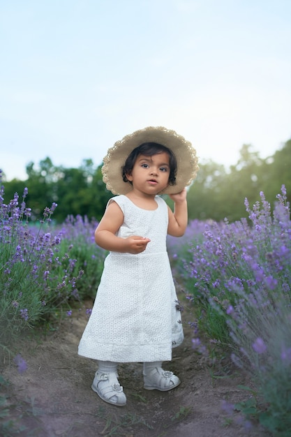 Bella bambina che indossa il cappello di paglia in posa nel campo di lavanda