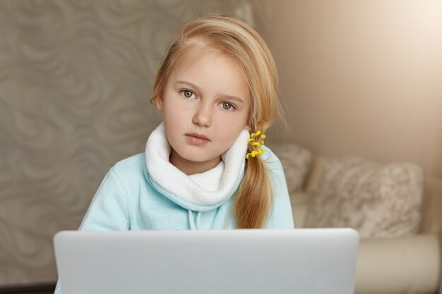 Bella bambina con capelli biondi, navigare in internet sul suo computer portatile