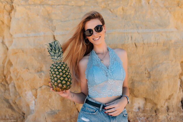 Bella bella donna con i capelli ricci è in possesso di ananas sulla spiaggia