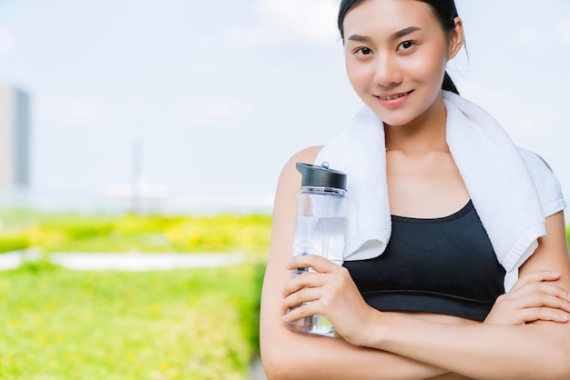 Bella bottiglia d'acqua della tenuta della mano della donna asiatica di sport per allenamento sano di yoga di forma fisica con il fondo del giardino