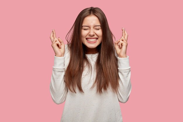 Bella bruna allegra felice che posa contro il muro rosa