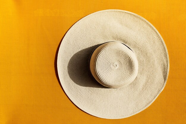 Bella cappello di paglia sul colore giallo vivace sfondo vivido. Vista dall&#39;alto.