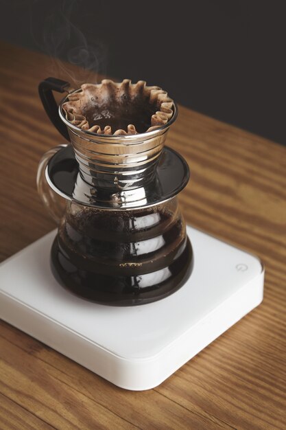 Bella close up di cromo trasparente a goccia macchina per il caffè con caffè filtrato tostato, isolato su spessa tavola di legno nella caffetteria. pesi bianchi. vapore. brutale.