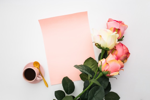 Bella composizione con caffè, rose rosa e carta bianca su bianco