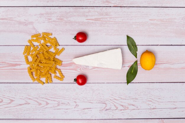 Bella composizione di pasta fusilli cruda; pomodori; formaggio; foglie di alloro e limone su fondo in legno