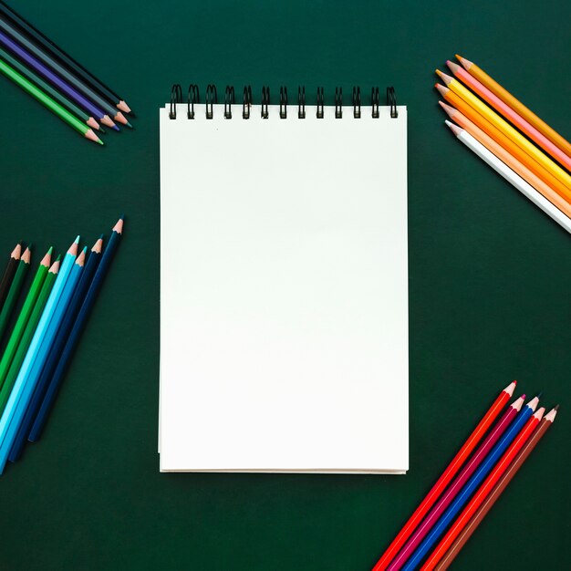 bella composizione piatta laici con notebook con matite colorate a bordo verde per tornare a scuola
