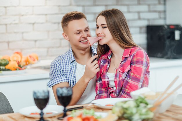 Bella coppia che tosta il prosciutto in cucina a casa. Tempo romantico.