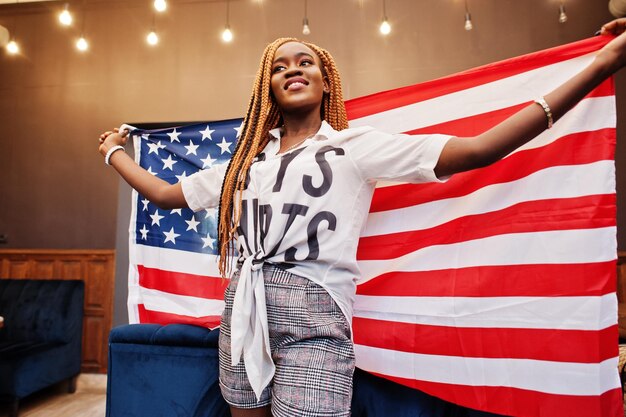 Bella donna africana in abiti casual eleganti in posa con la bandiera degli Stati Uniti a portata di mano in ufficio