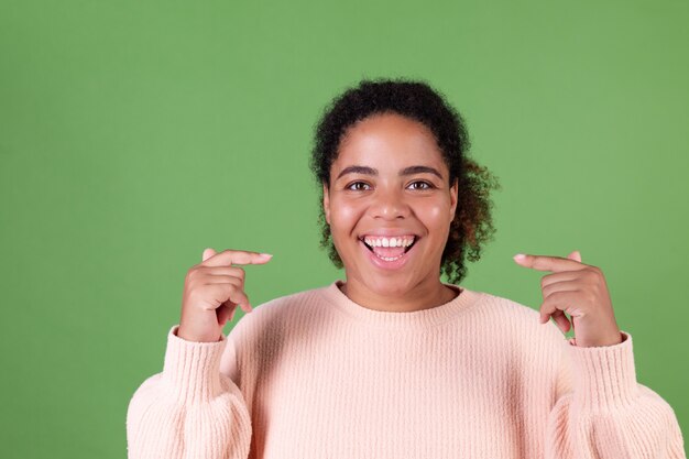 Bella donna afroamericana sulla parete verde allegro sorridente punto di indice sui denti bianchi sorriso